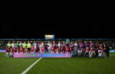 I giocatori di due squadre di calcio posano con dei bambini, alcuni in sedia a rotelle, dietro uno striscione di sensibilizzazione sulle malattie rare.