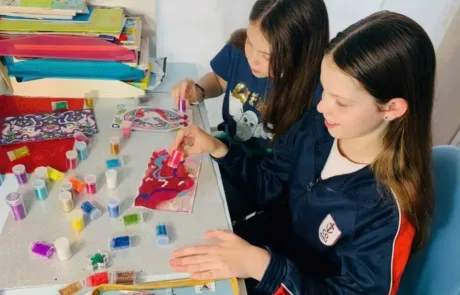 Due alunne del COAMI applicano glitter colorato sui loro disegni in classe.