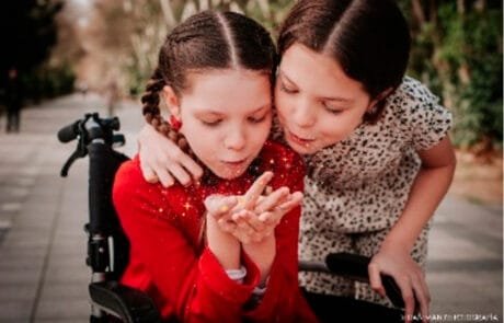 Carolina, sulla sua sedia a rotelle, e sua sorella Isabel soffiano insieme una manciata di glitter.