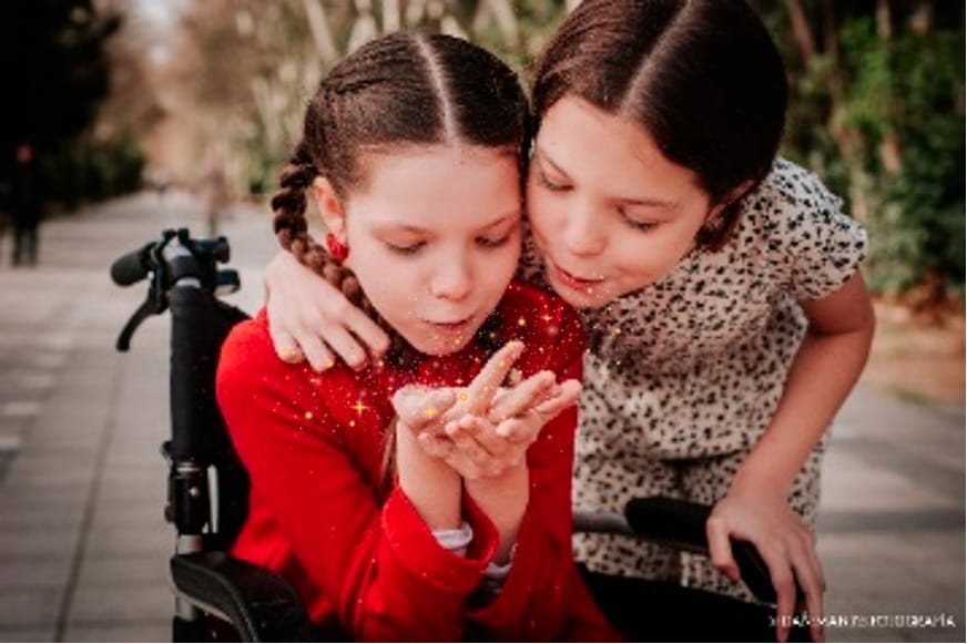 Carolina, sulla sua sedia a rotelle, e sua sorella Isabel soffiano insieme una manciata di glitter.