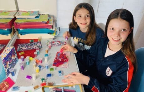 Carolina e una compagna decorano con il glitter dei disegni di unicorni a scuola.