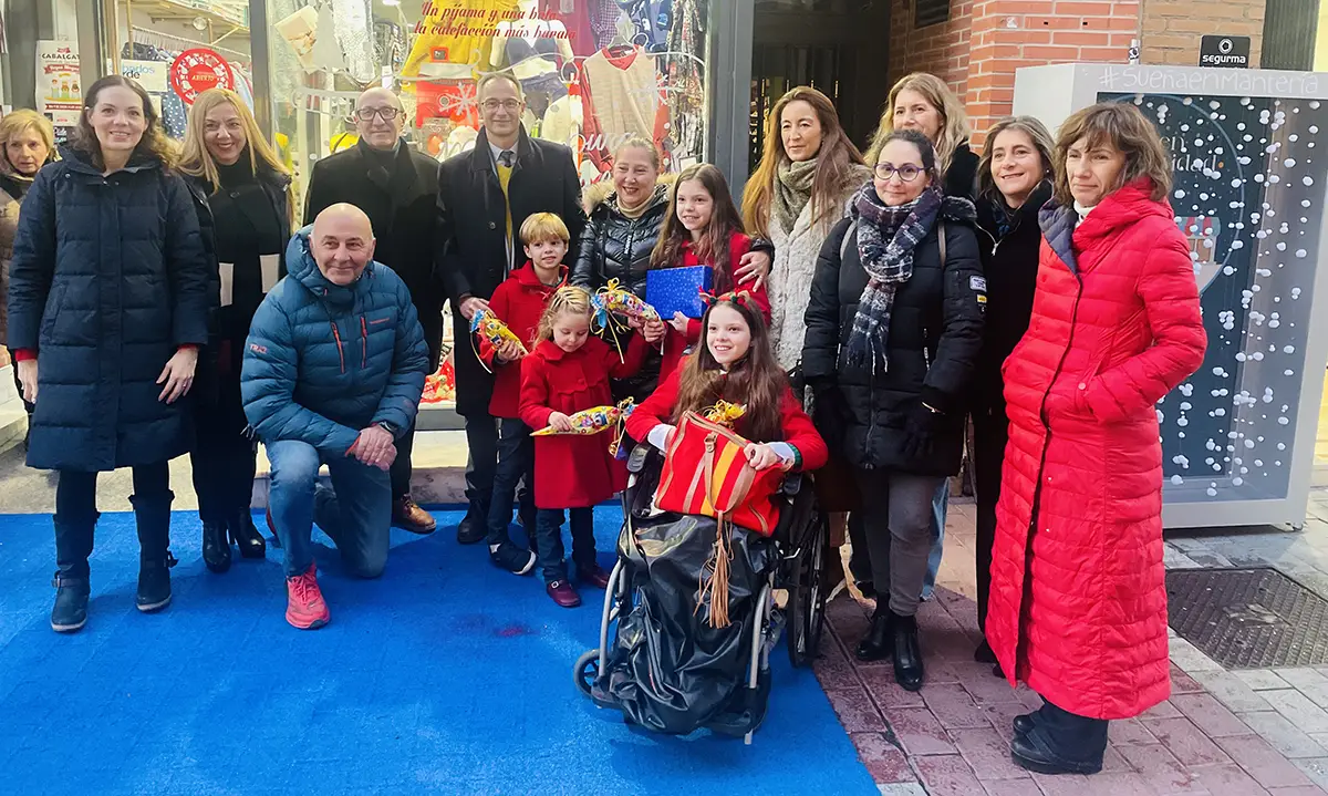 Foto di gruppo davanti a un negozio della calle Mantería decorato per Natale, con una bambina in sedia a rotelle al centro.