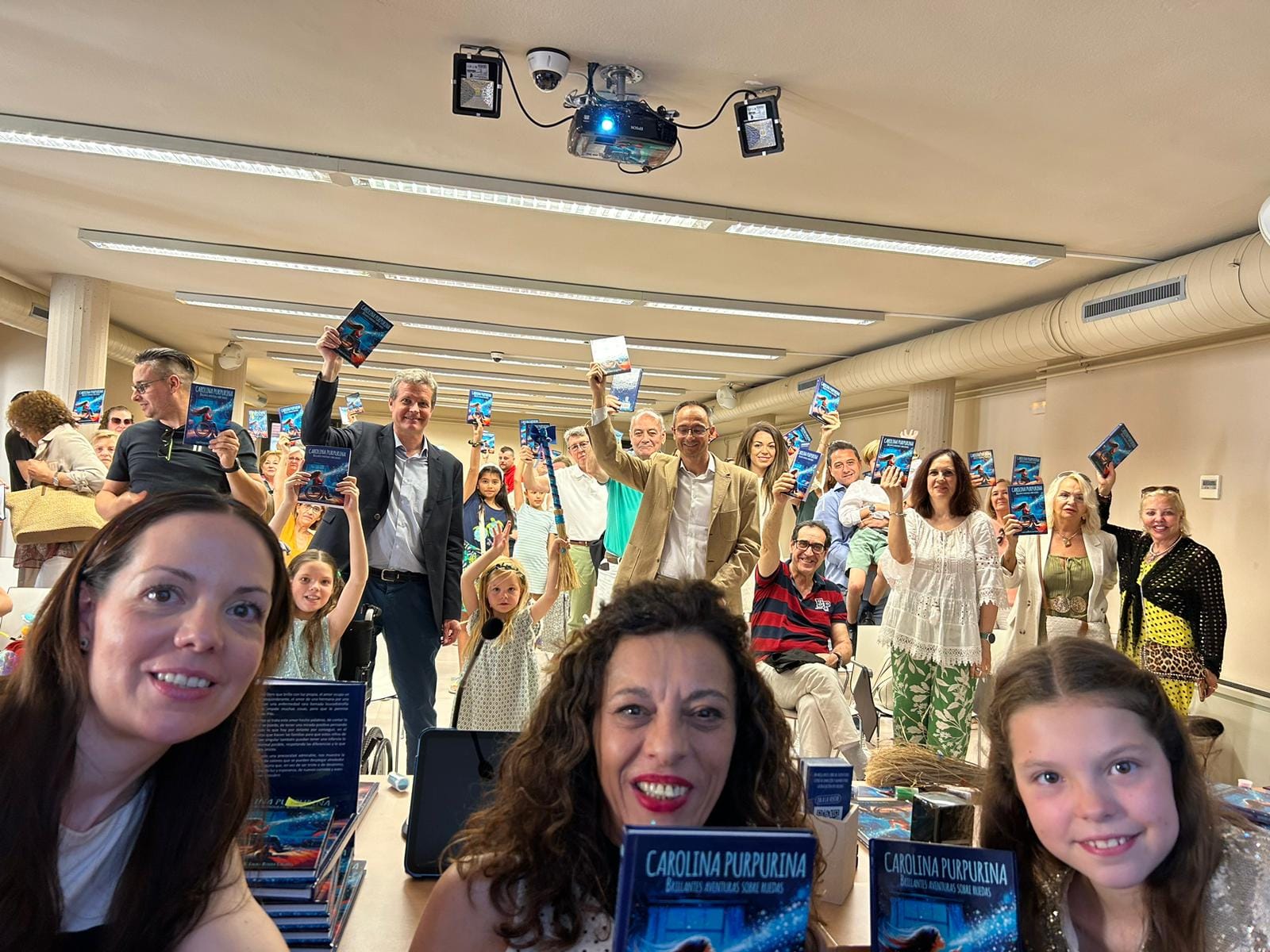 Selfie alla presentazione: il pubblico solleva copie di «Carolina Purpurina» sopra un tavolo pieno di libri.