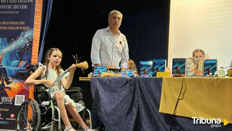 Presentazione in un'aula magna: una bambina in sedia a rotelle con una scopa di saggina, accanto al tavolo delle copie.