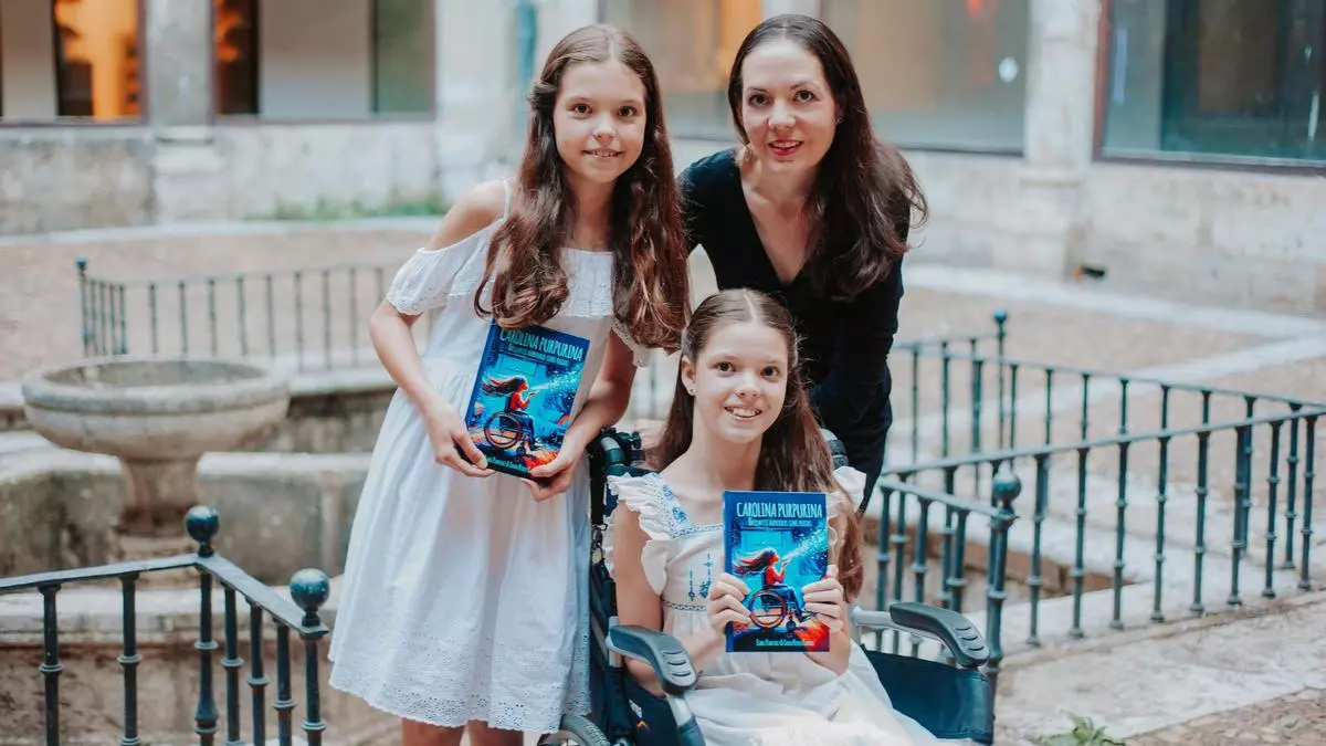 In un cortile, una bambina in sedia a rotelle e un'altra in piedi mostrano la copertina di «Carolina Purpurina» accanto a una donna.