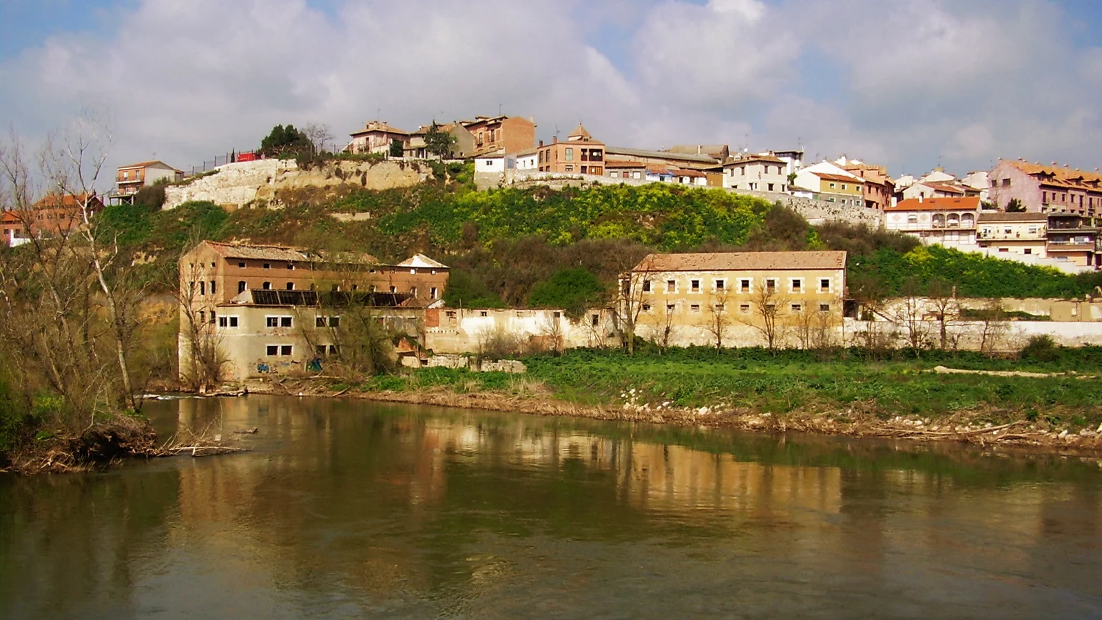 Veduta di un paese adagiato su una collina accanto a un fiume, con edifici antichi sulla riva.