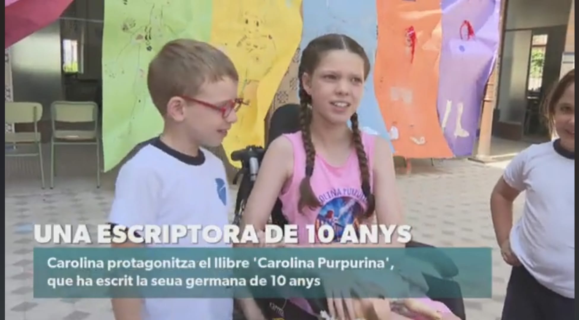 Fotogramma del telegiornale di À Punt: Carolina, con la maglietta del libro, conversa con un bambino nel cortile della scuola.