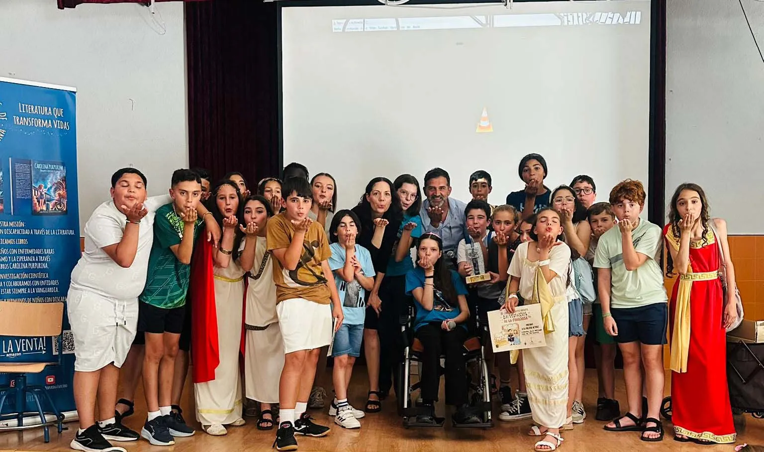 Alunni e insegnanti soffiano glitter attorno a Carolina, che tiene il diploma accanto al trofeo.