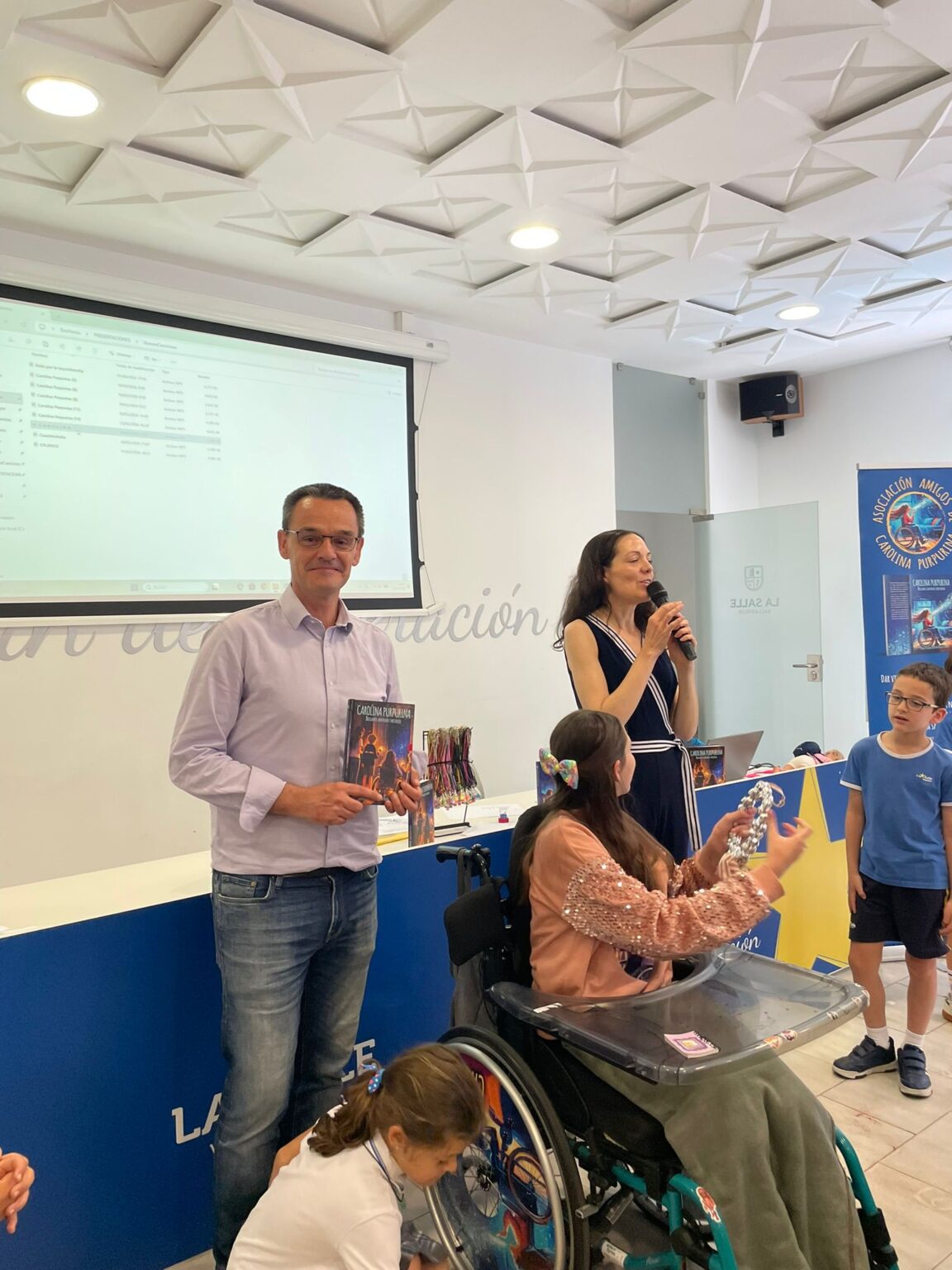 Presentazione a La Salle Valladolid: Laura parla al microfono mentre il libro viene mostrato agli alunni.