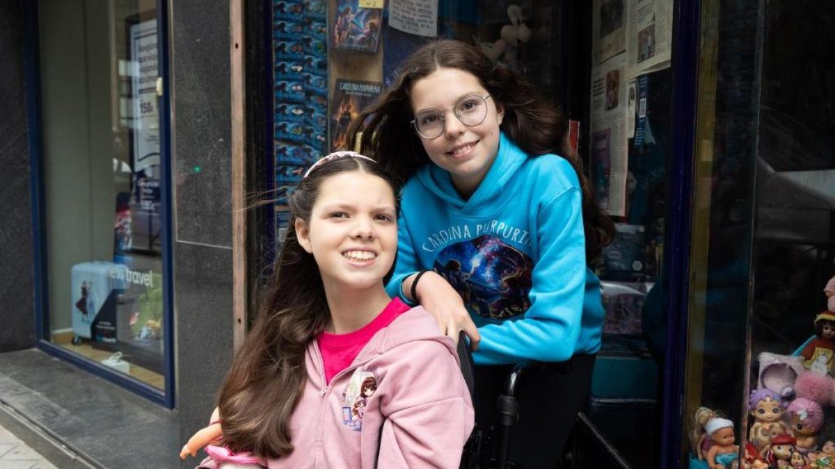 Carolina, sulla sedia a rotelle, e Isabel, con la felpa di Carolina Purpurina, posano davanti a una vetrina con i libri della saga.