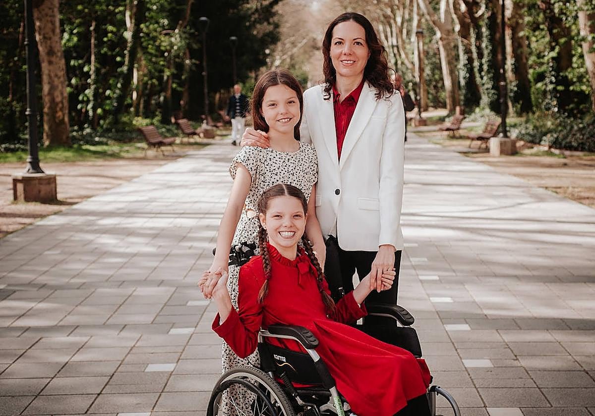Carolina, sulla sedia a rotelle e con un vestito rosso, posa con la sua famiglia in un viale alberato di un parco.