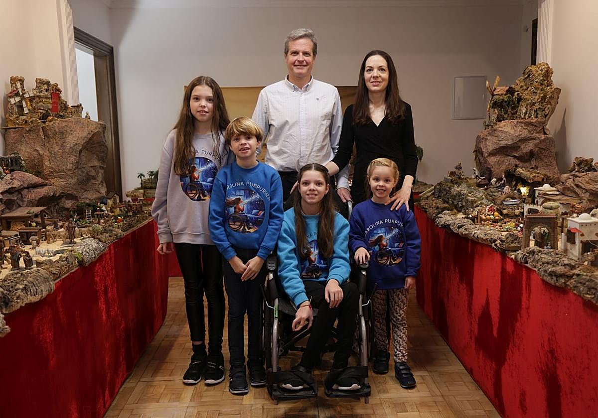 Due adulti e quattro bambini con felpe di Carolina Purpurina posano tra i tavoli del presepe; al centro Carolina, sulla sedia a rotelle.