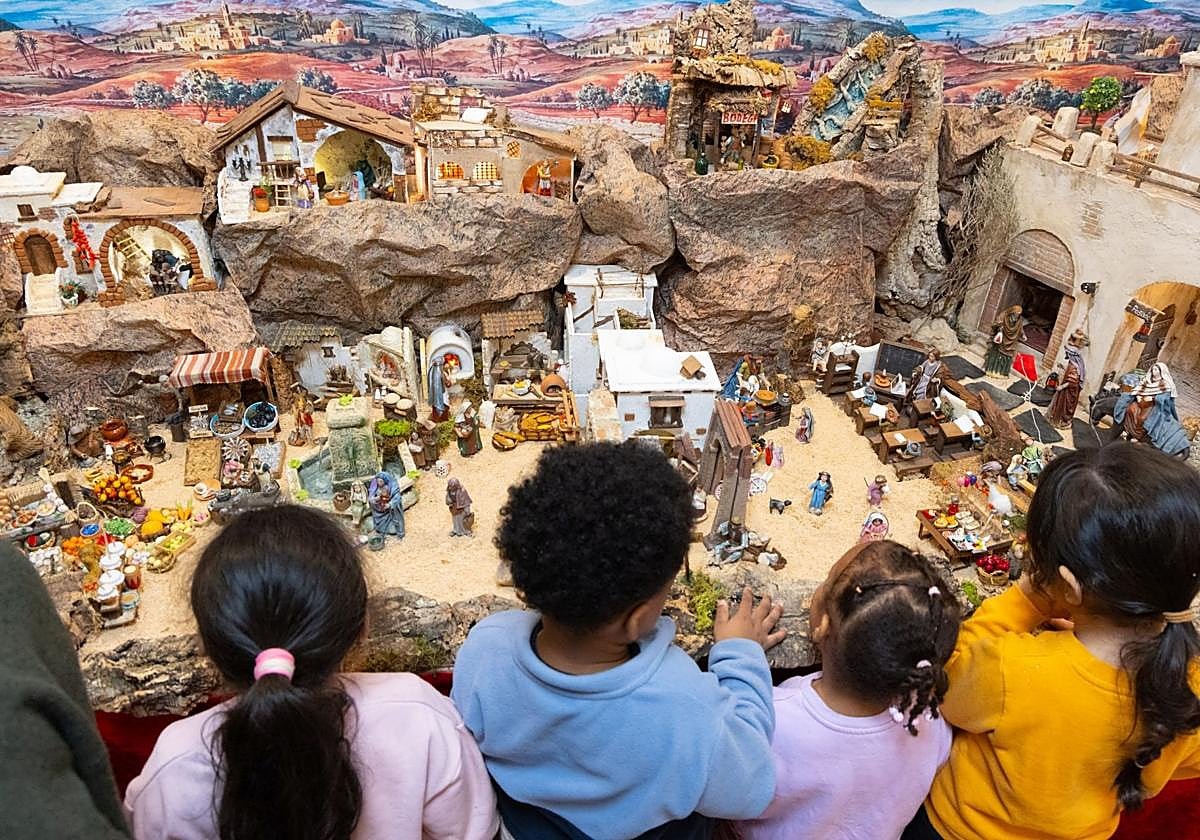 I primi visitatori del presepe: quattro bambini, di spalle, si affacciano sul suo paesaggio di rocce, case e statuine.