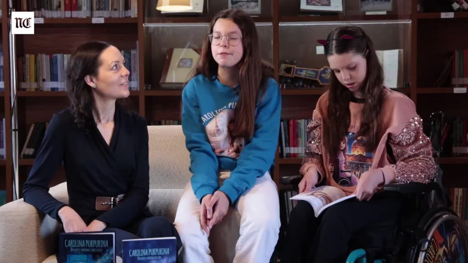Intervista sul terzo libro: Laura e Isabel sedute dietro due libri di Carolina Purpurina, e Carolina, sulla sedia a rotelle, che ne sfoglia uno.